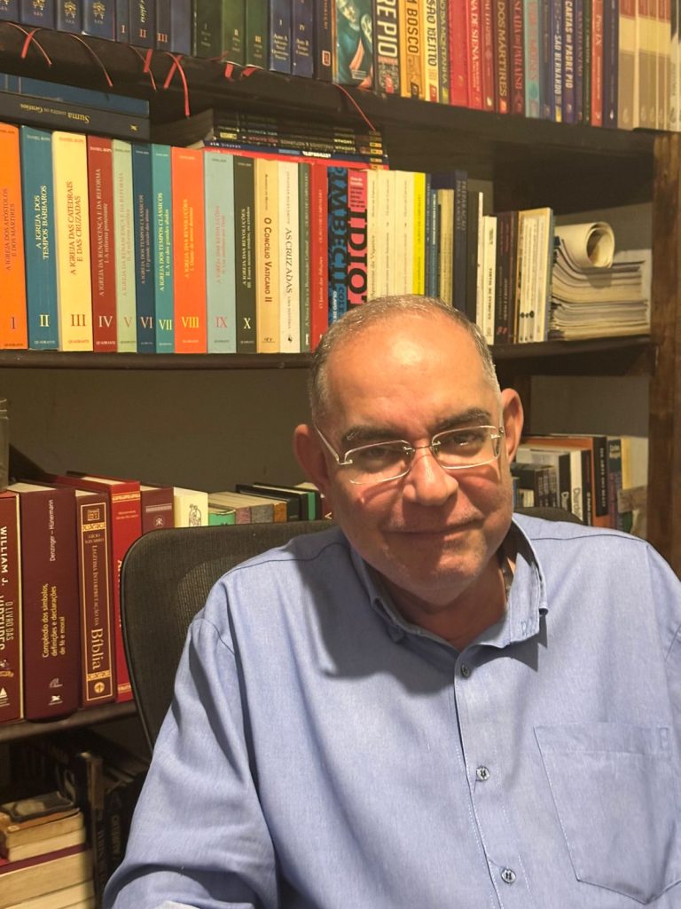 Tarcísio na frente de sua estante de livros onde é possível ver dois livros do escritor Olavo de Carvalho (Créditos: Catharina Moura)